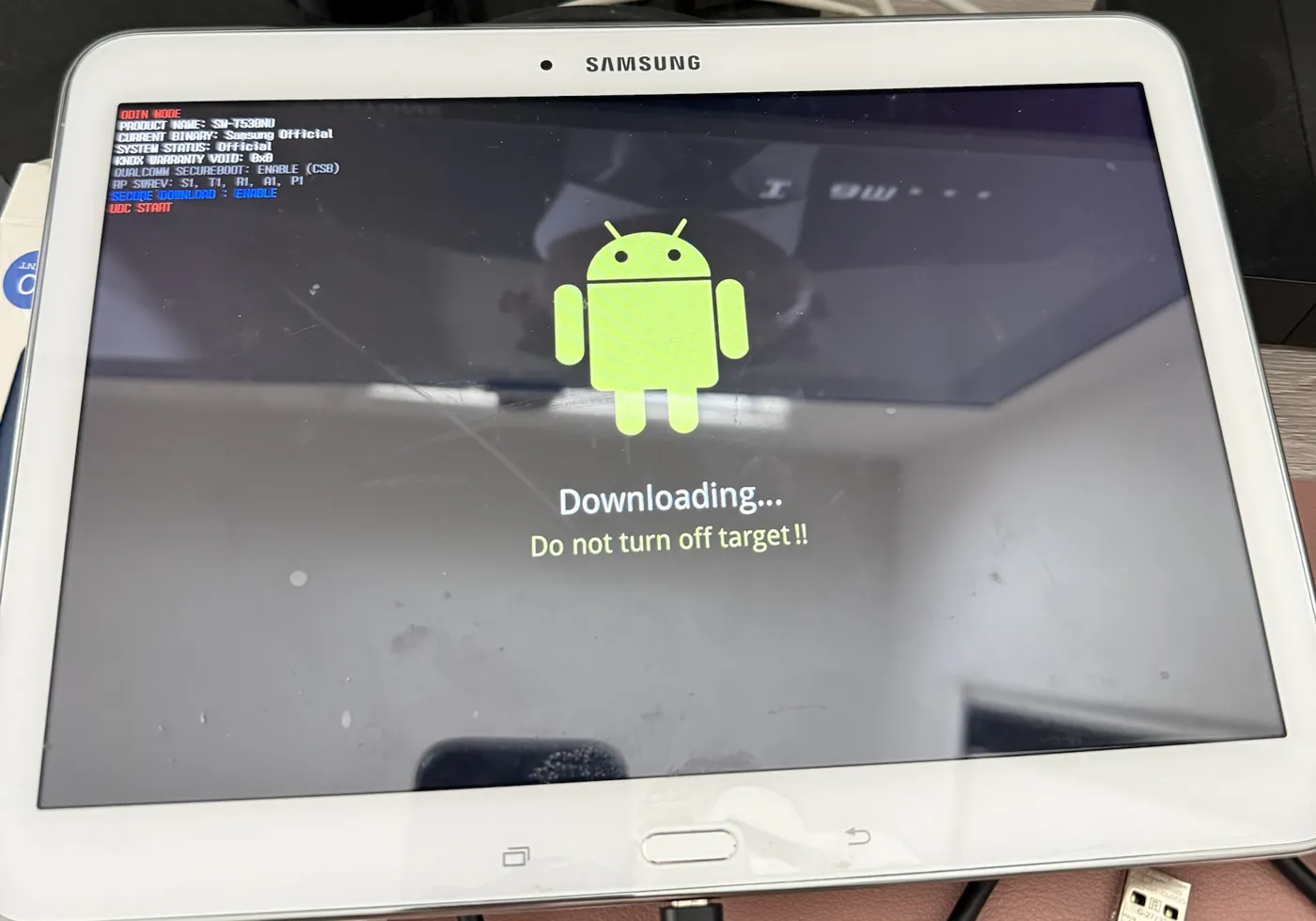 Samsung tablet in Odin download mode showing an Android robot and Downloading
